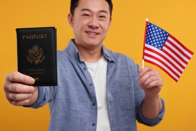 Immigration. Happy man with passport and American flag on orange background, selective focus