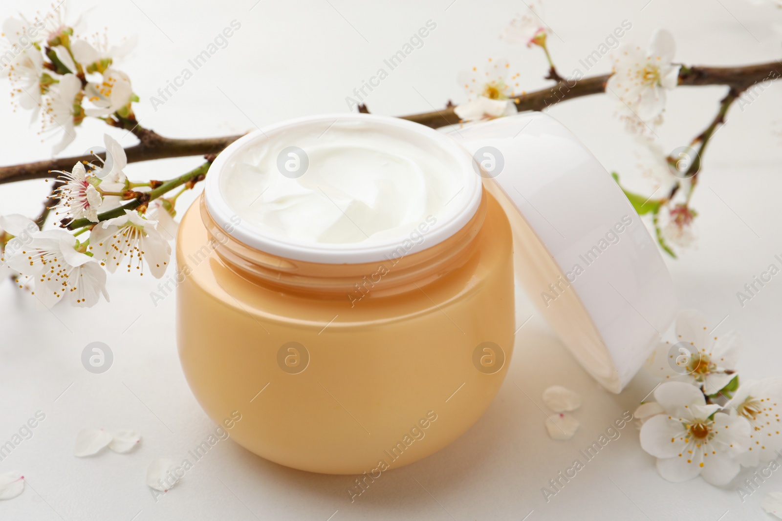 Photo of Jar of face cream, tree branch and flowers on white marble table