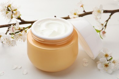 Jar of face cream, tree branch and flowers on white marble table