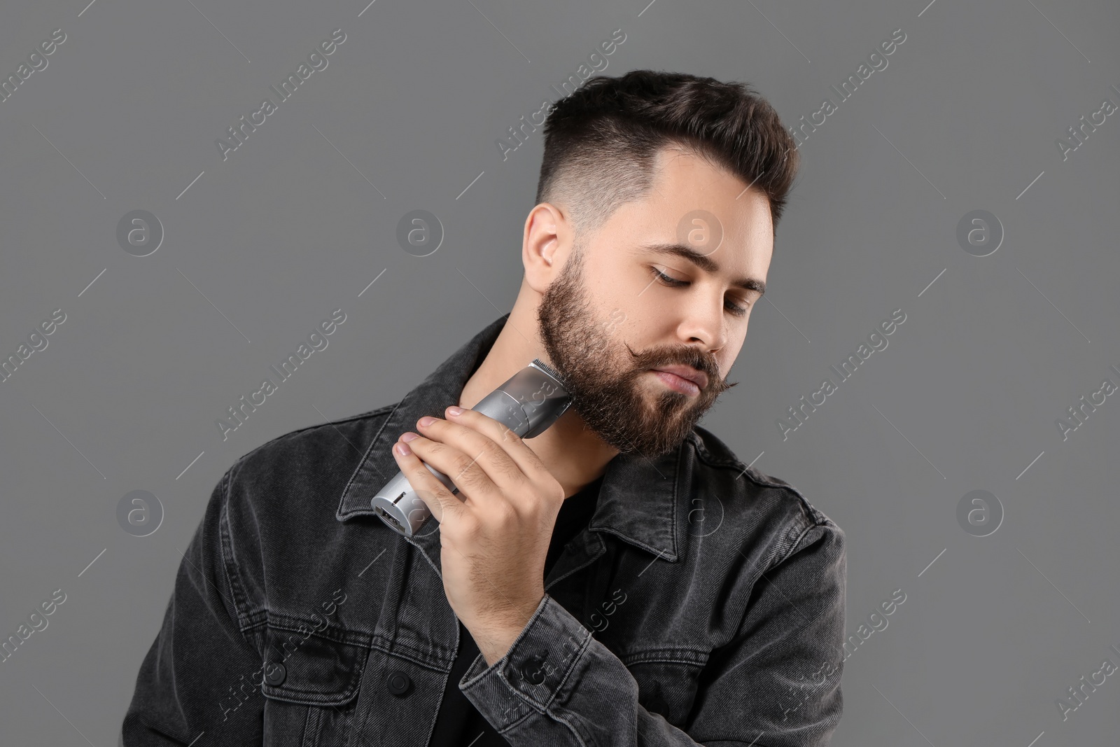 Photo of Handsome young man trimming beard on grey background