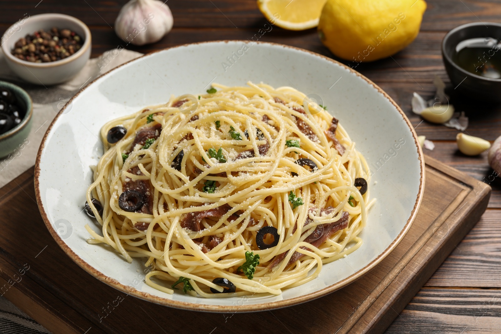 Photo of Delicious pasta with anchovies, olives and parmesan cheese served on wooden table