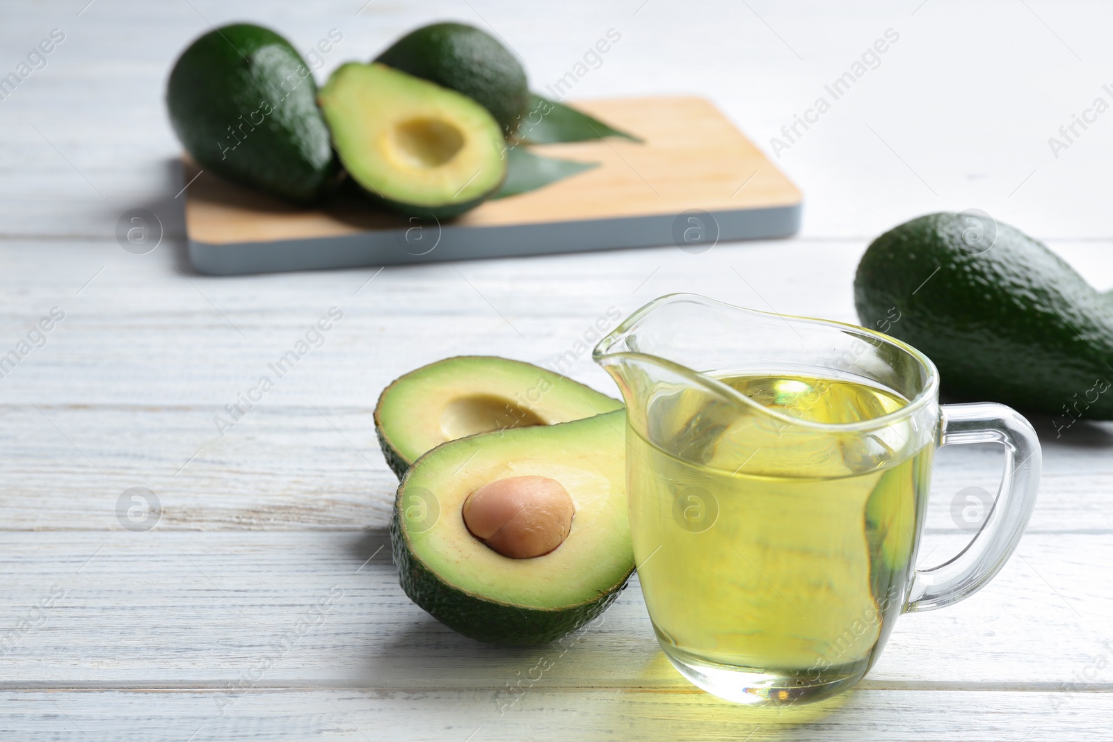 Photo of Jug of natural oil and avocados on white wooden background. Space for text