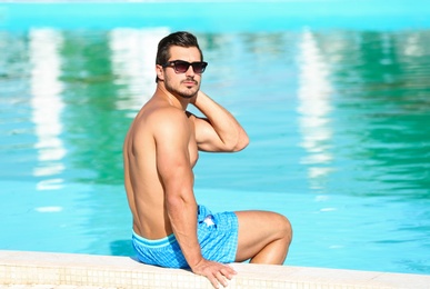 Photo of Handsome young man sitting at swimming pool edge on sunny day