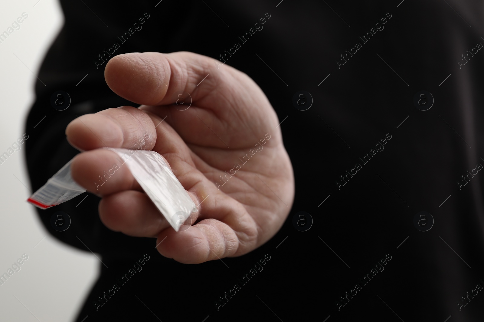 Photo of Drug addiction. Man with plastic bag of cocaine on light background, closeup