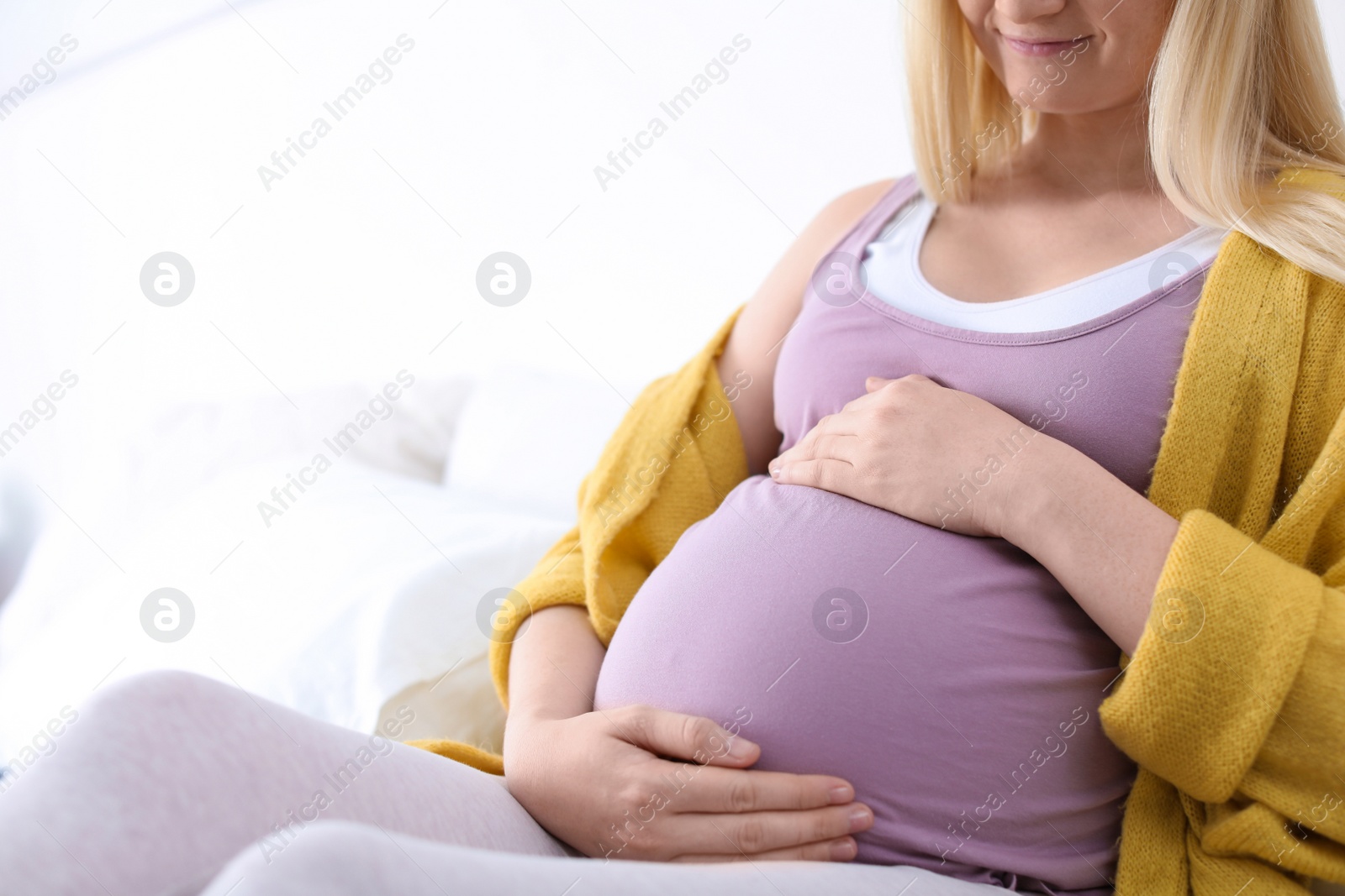 Photo of Pregnant woman resting on bed in light room, closeup. Space for text