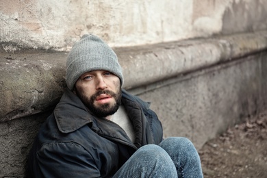 Photo of Poor homeless man sitting near wall on street. Space for text