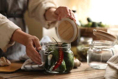Photo of Woman pickling glass jar of cucumbers at wooden table, closeup