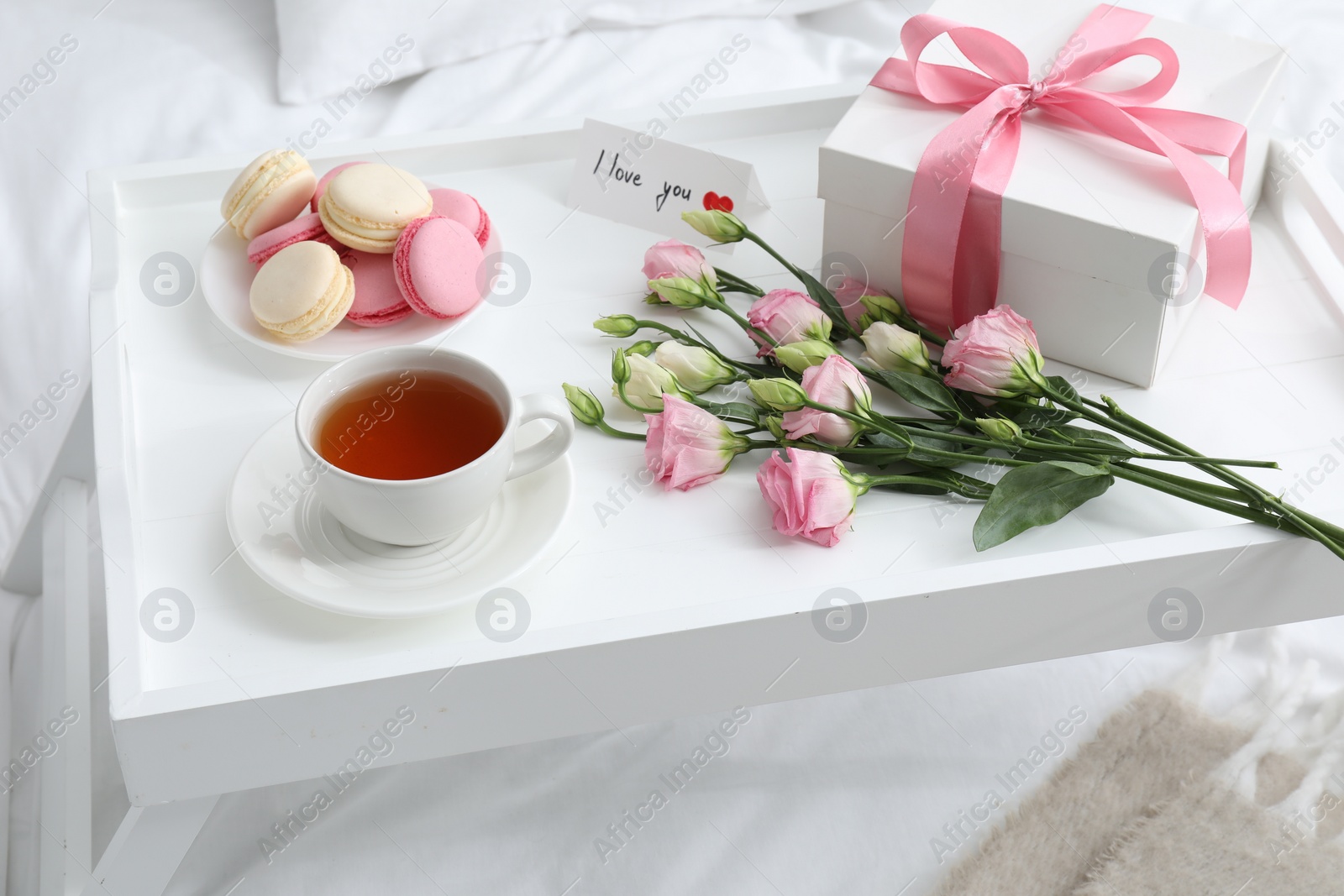 Photo of Tasty breakfast served in bed. Delicious macarons, tea, gift box, flowers and I Love You card on tray