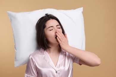 Photo of Sleepy young woman with pillow yawning on beige background. Insomnia problem