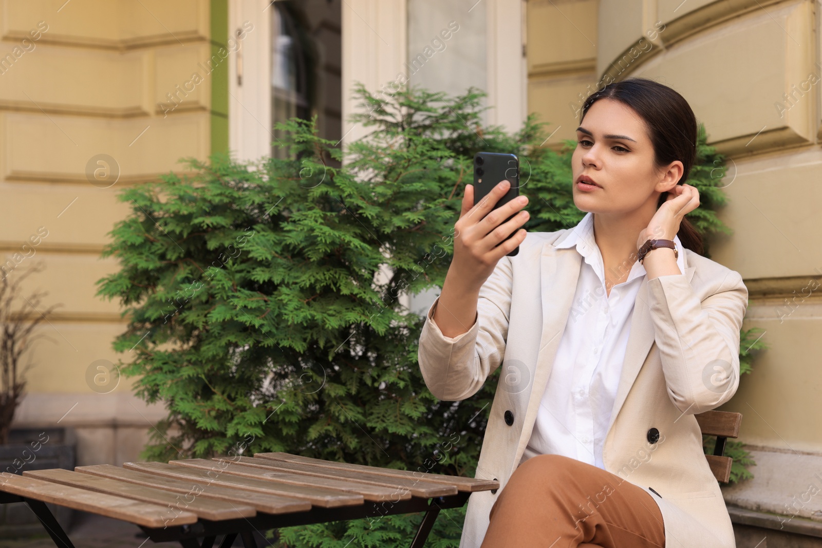 Photo of Beautiful young woman using smartphone at table in outdoor cafe