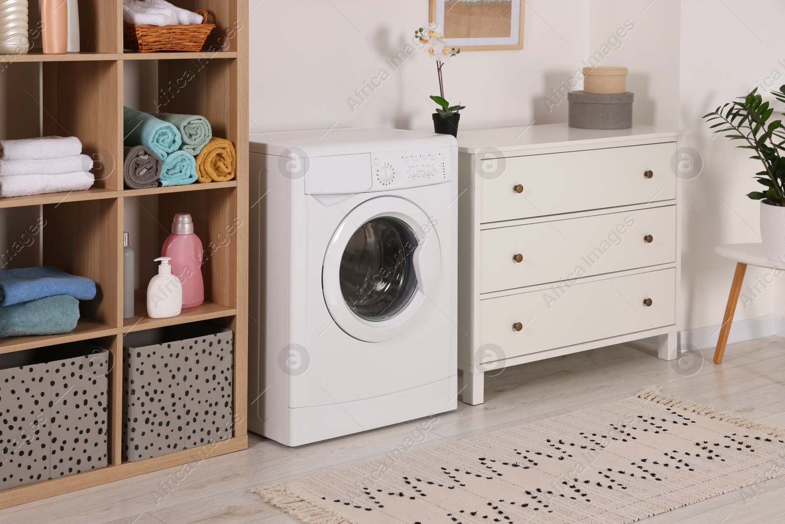 Photo of Stylish laundry room with washing machine and chest of drawers. Interior design