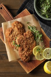 Photo of Tasty schnitzels served with lemon and microgreens on wooden table, flat lay