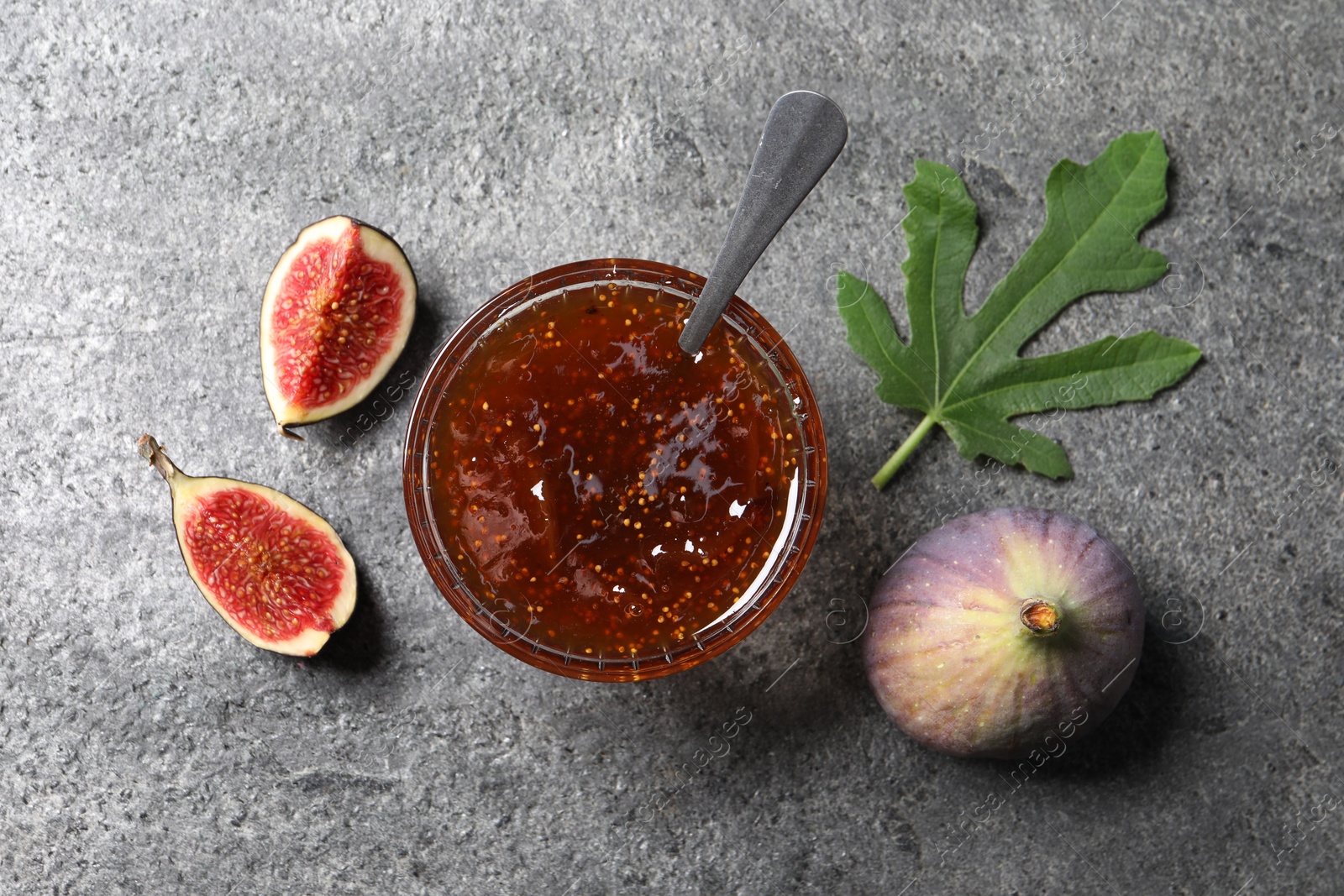 Photo of Glass bowl with tasty sweet jam and fresh figs on grey table, flat lay