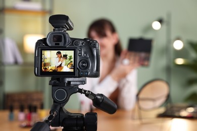 Beauty blogger recording video while showing eyeshadow palette at home, focus on camera