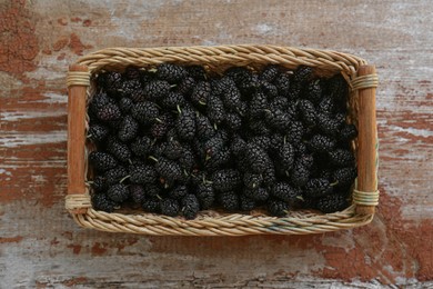 Photo of Wicker basket with delicious ripe black mulberries on wooden table, top view