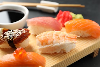 Photo of Wooden board with delicious nigiri sushi and soy sauce on black table, closeup