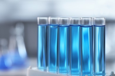 Photo of Test tubes with light blue liquid on blurred background, closeup