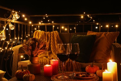 Glasses of wine, burning candles and autumn decor on outdoor terrace in evening