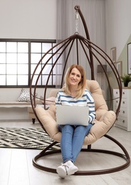 Photo of Young woman working with laptop on hanging armchair in home office