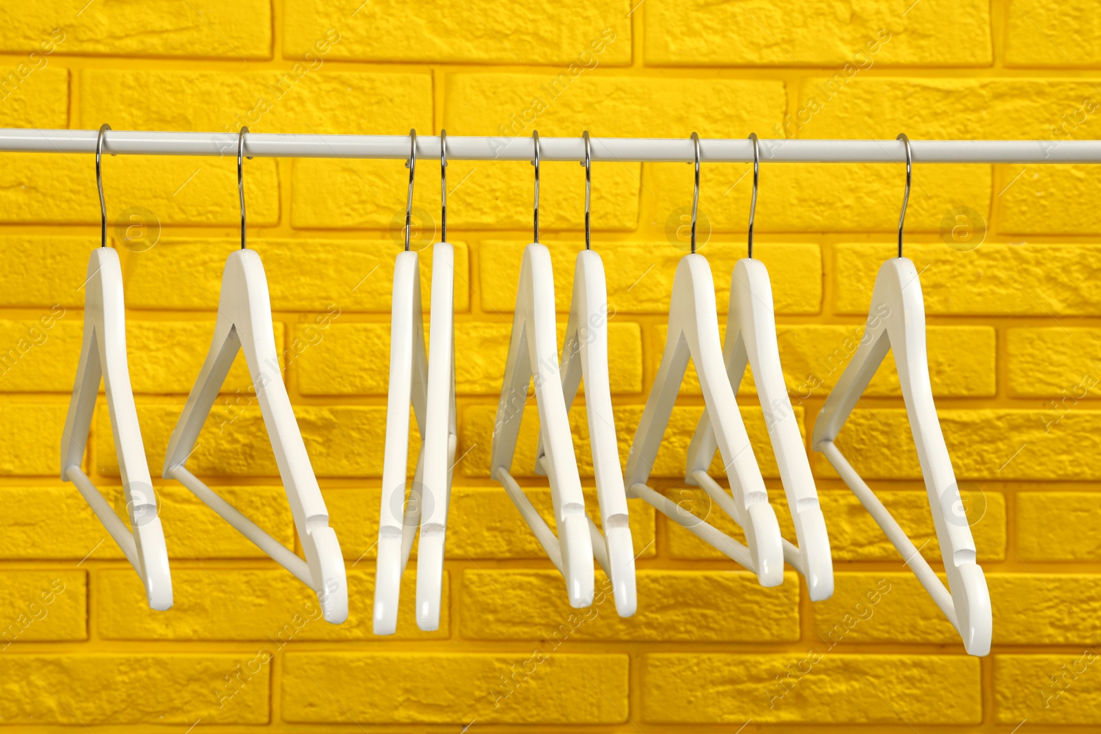 Photo of Wardrobe rack with many hangers near yellow brick wall