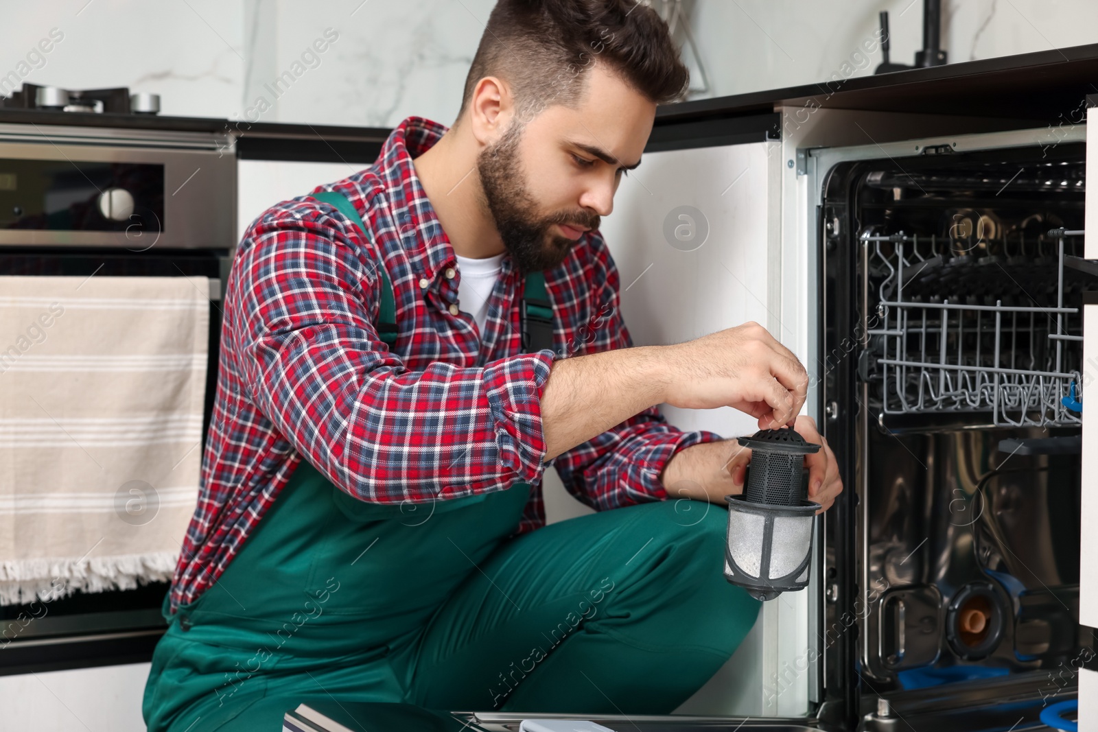 Photo of Repairman holding drain filter near dishwasher in kitchen