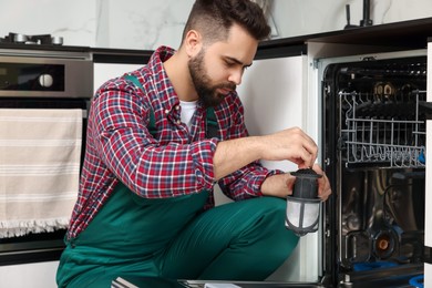 Repairman holding drain filter near dishwasher in kitchen