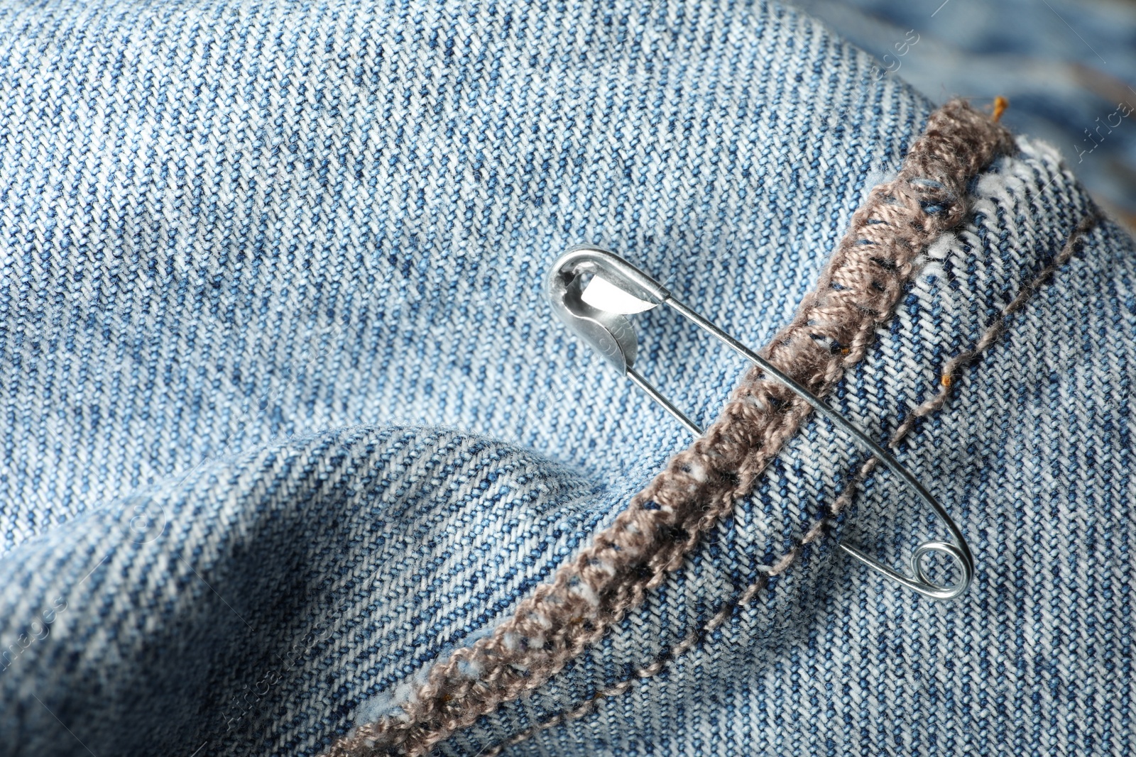 Photo of Metal safety pin on denim fabric, closeup