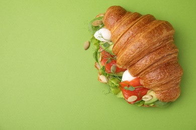 Photo of Tasty croissant with salmon, avocado, mozzarella and lettuce on green background, top view. Space for text