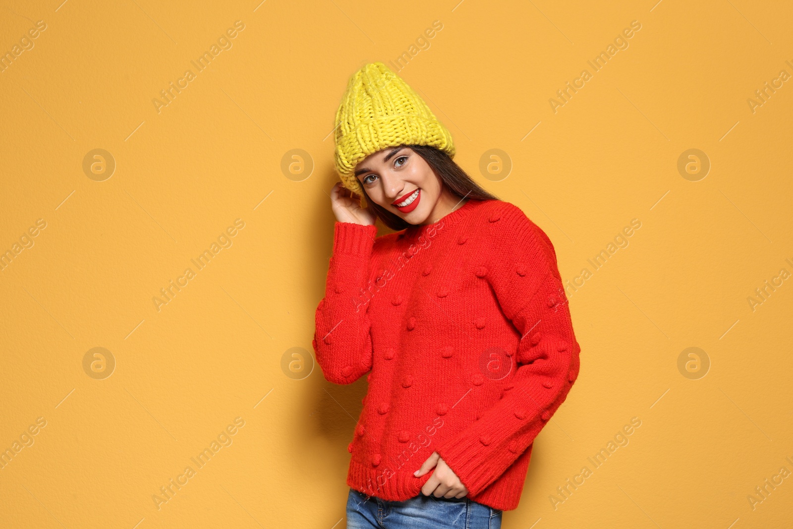 Photo of Young woman in warm sweater and knitted hat on color background. Celebrating Christmas