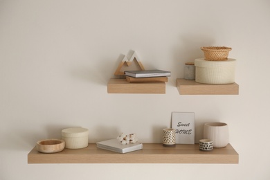 Wooden shelves with books and different decorative elements on light wall