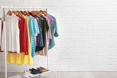 Photo of Wardrobe rack with stylish clothes and shoes near brick wall indoors. Space for text