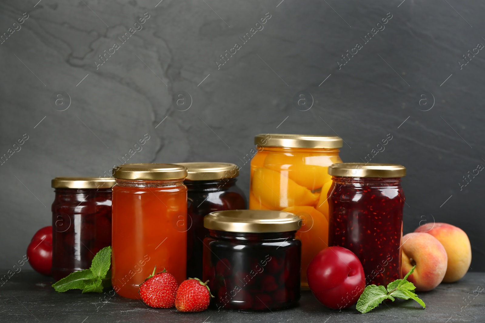 Photo of Jars of pickled fruits and jams on grey table