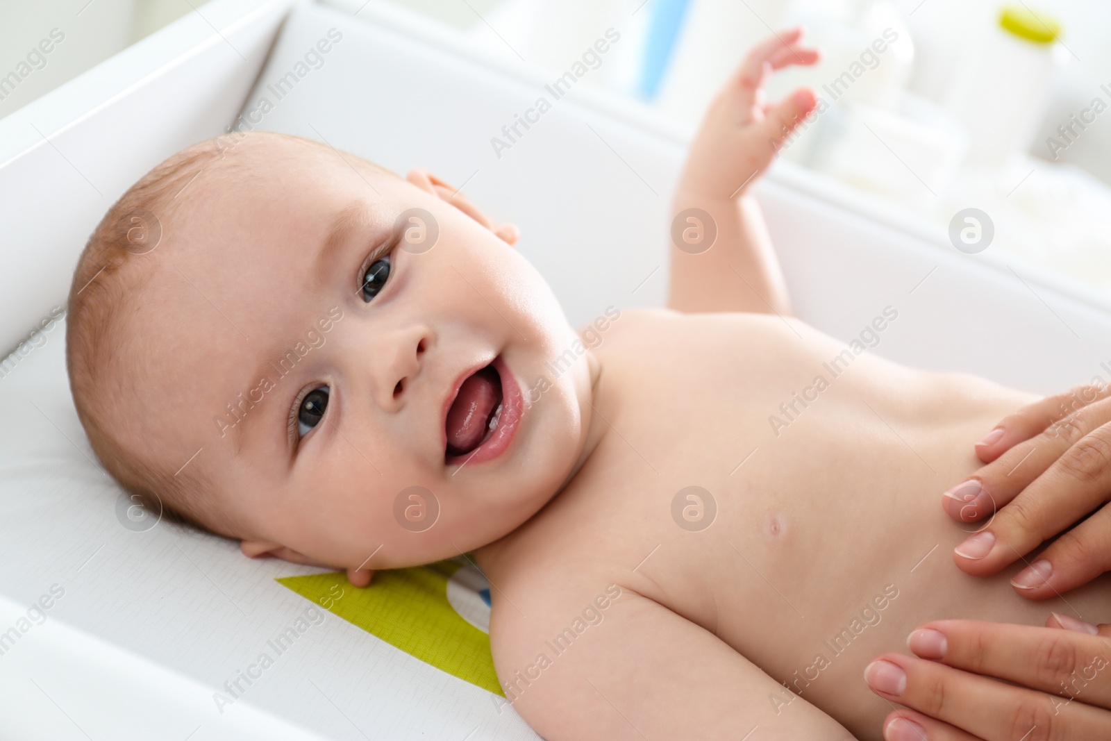 Photo of Young woman massaging cute baby on changing table