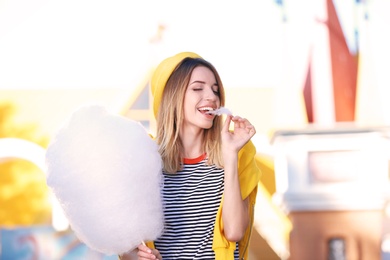 Photo of Young cheerful woman having fun with  cotton candy in amusement park