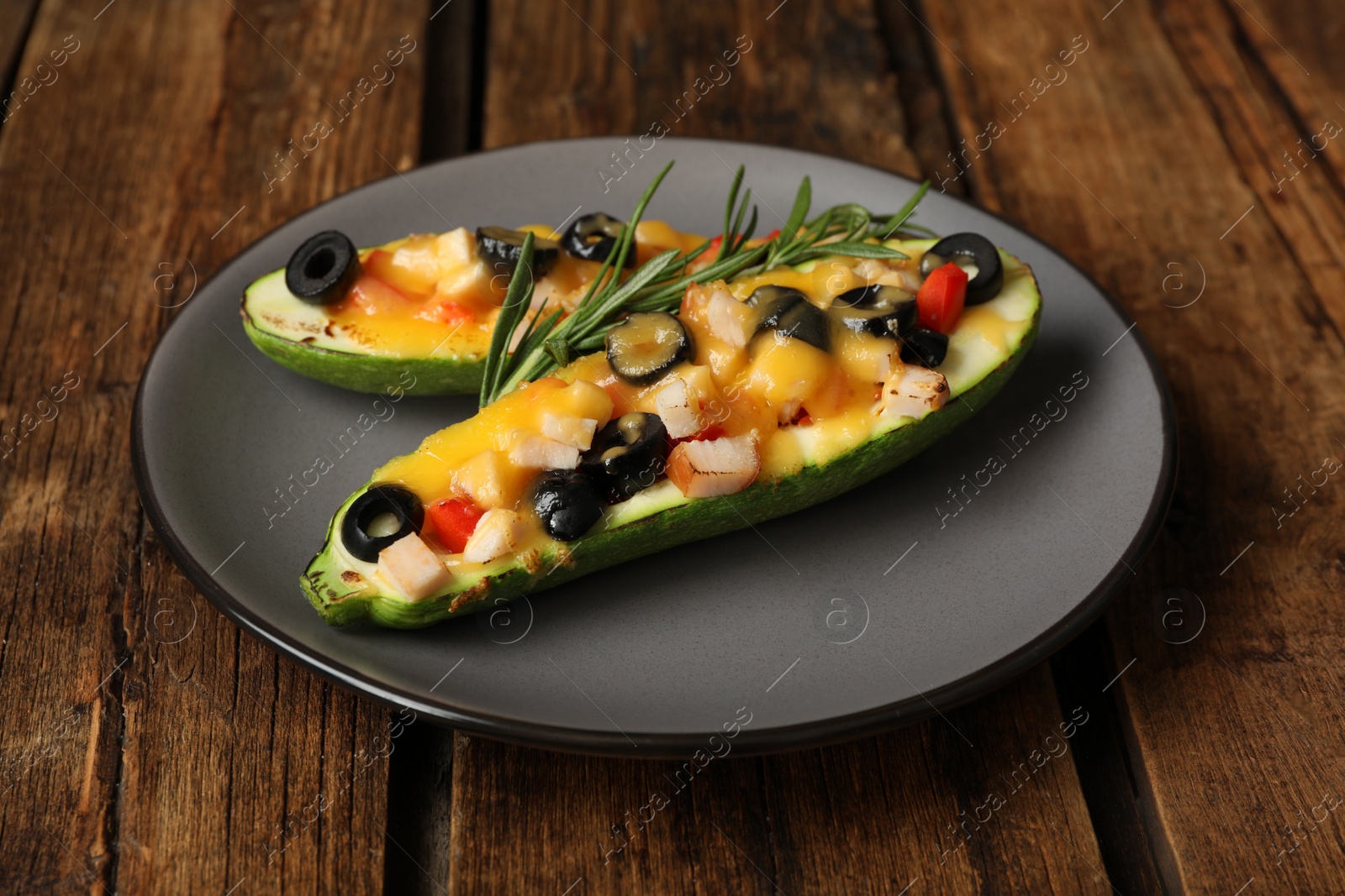 Photo of Plate of baked stuffed zucchinis served on wooden table, closeup