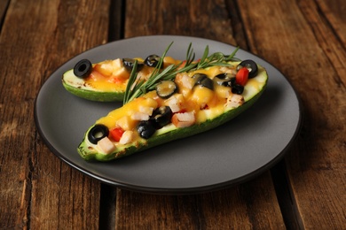 Photo of Plate of baked stuffed zucchinis served on wooden table, closeup