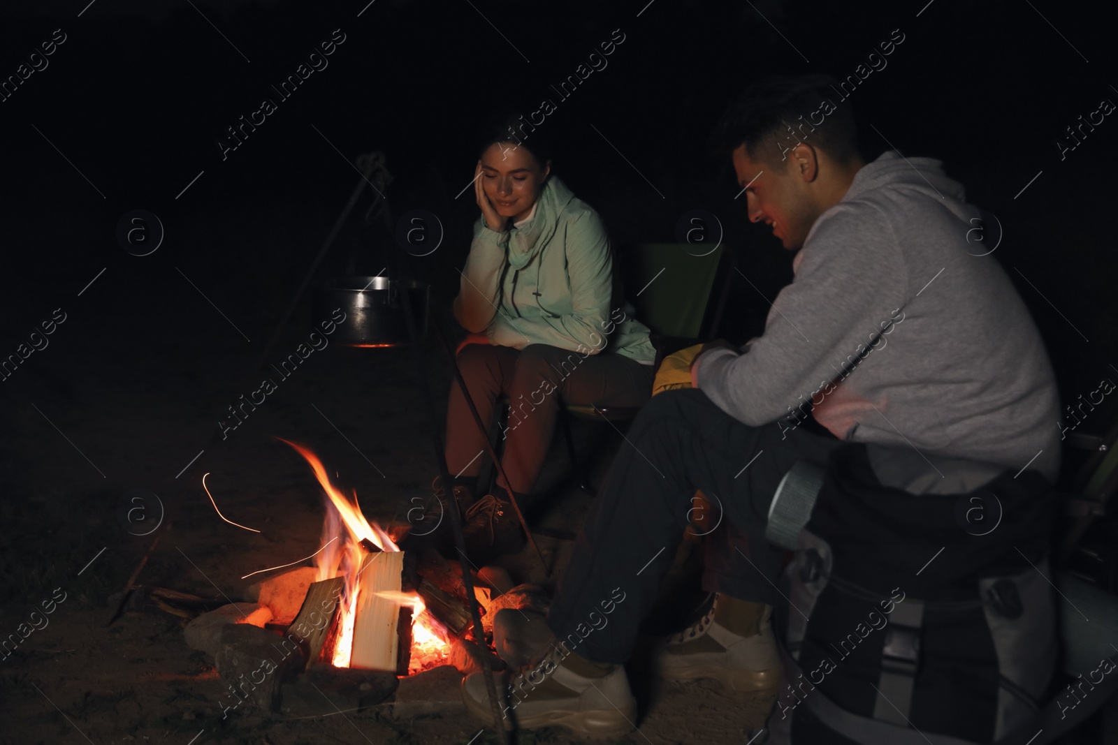 Photo of Couple near bonfire outdoors in evening. Camping season