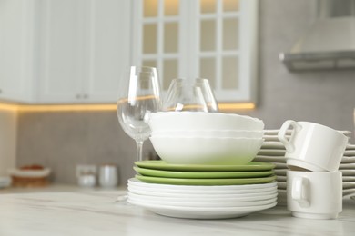 Clean plates, bowls, cups and glasses on white marble table in kitchen