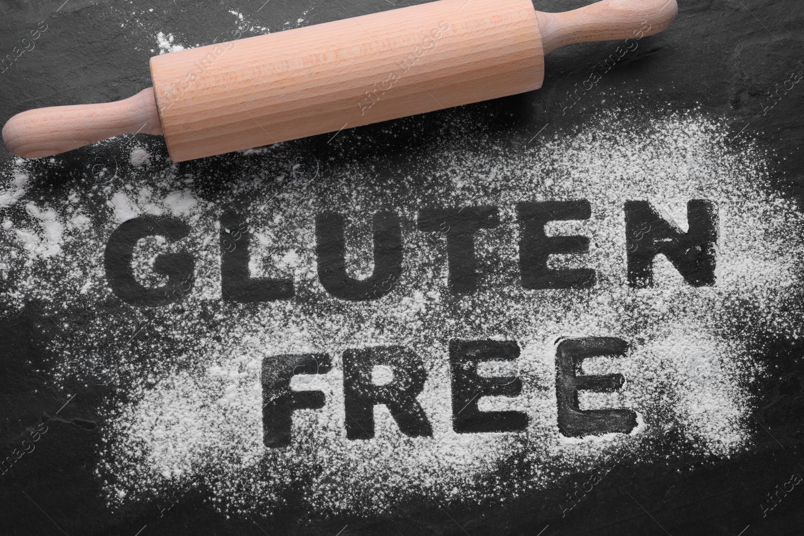 Photo of Rolling pin and phrase Gluten free written with flour on black table, flat lay