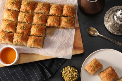 Photo of Delicious sweet baklava with pistachios and honey on black table, flat lay