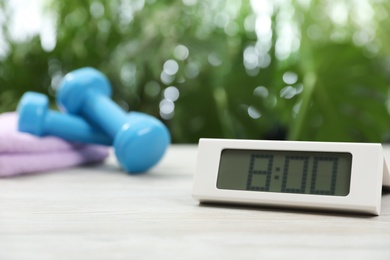 Photo of Digital alarm clock on white wooden table outdoors, space for text. Morning exercise