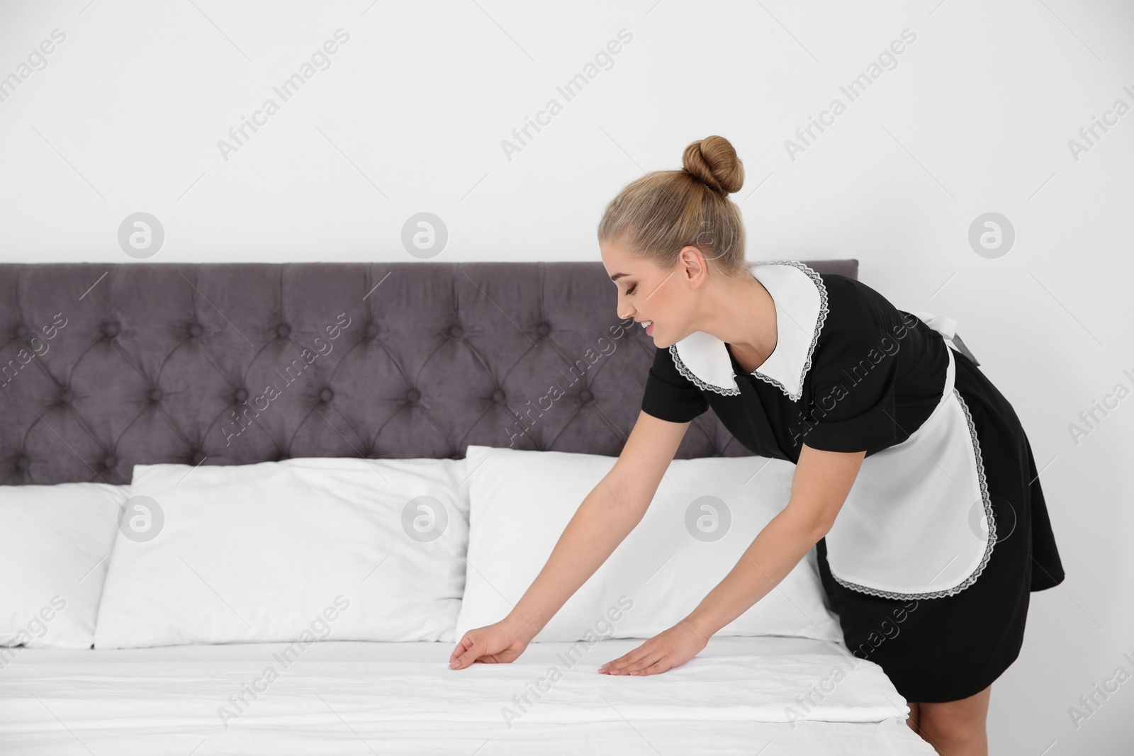 Photo of Young chambermaid making bed in hotel room