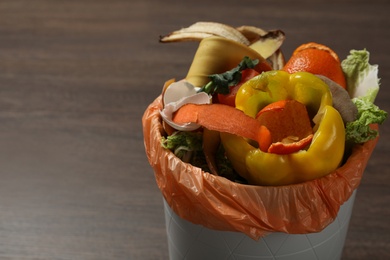 Photo of Trash bin with organic waste for composting on wooden background, closeup