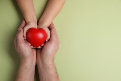 Photo of Father and his child holding red decorative heart on light green background, top view. Space for text