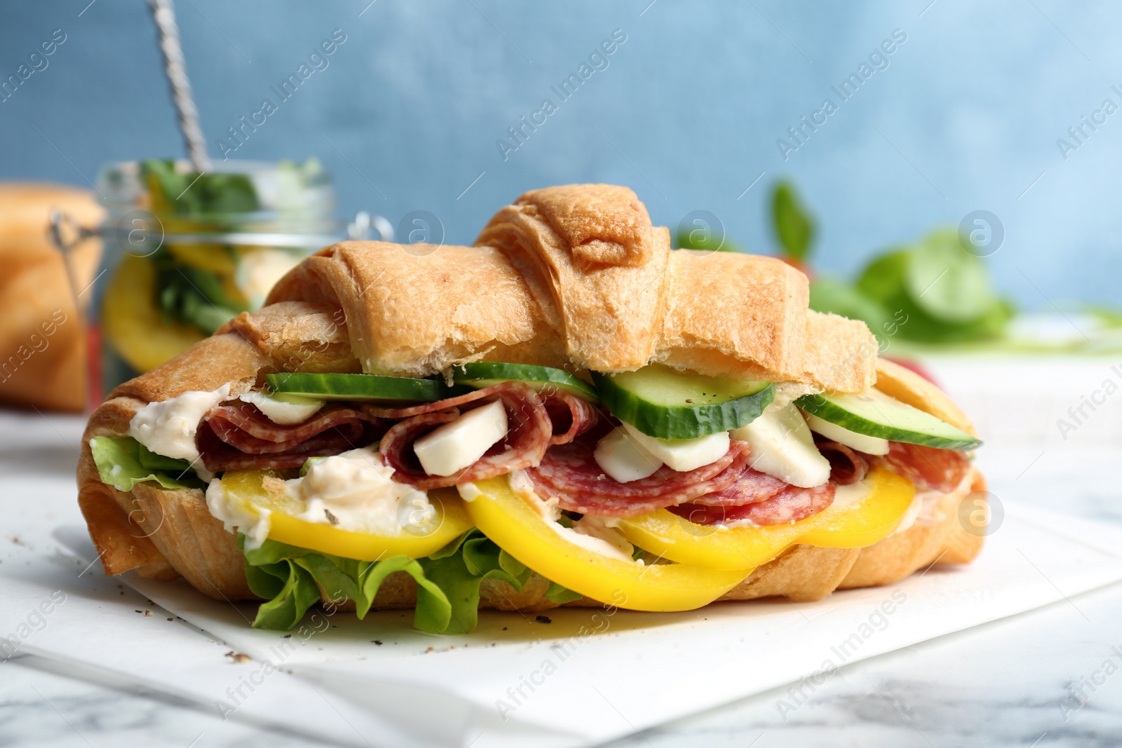 Photo of Tasty croissant sandwich with salami on table