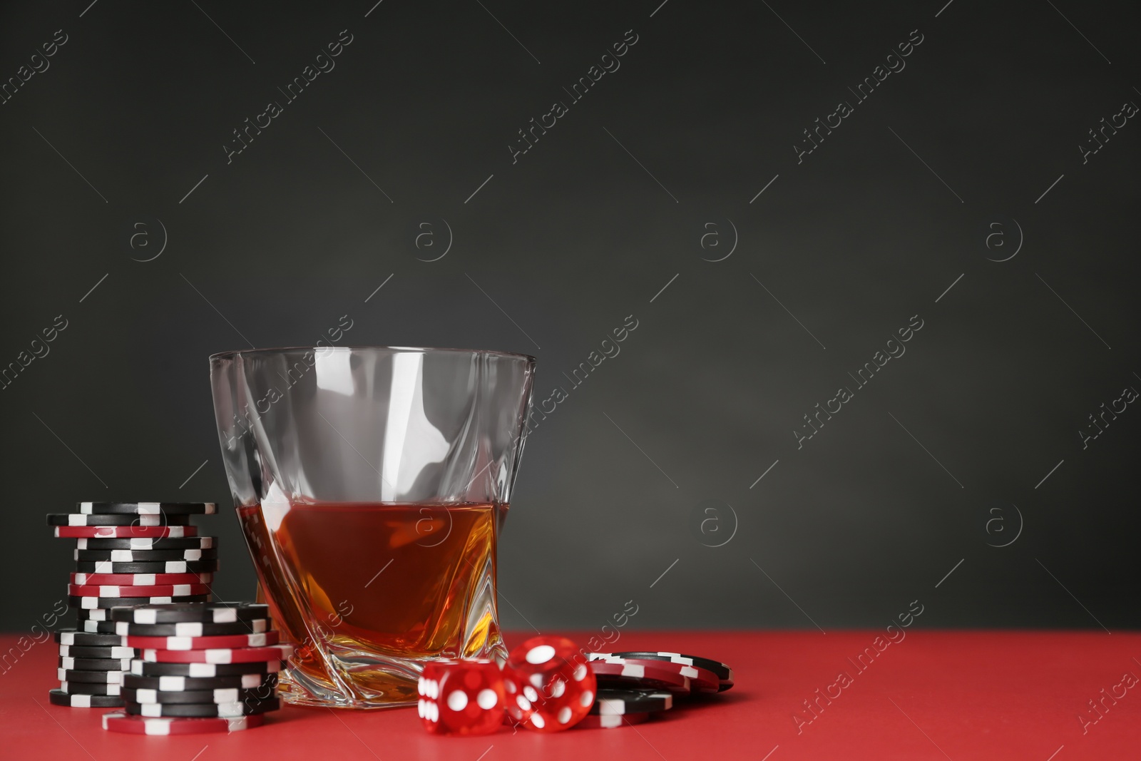 Photo of Casino chips, dice and whiskey on red table, space for text