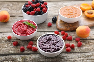 Photo of Different puree in bowls and fresh fruits on wooden table