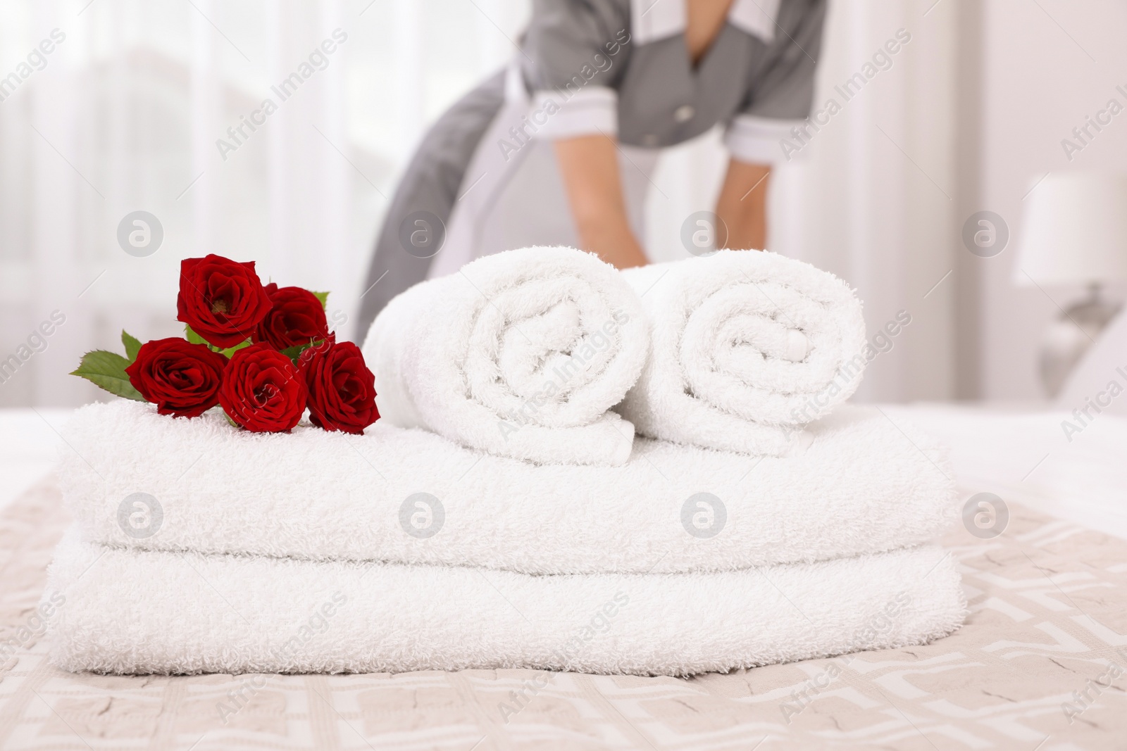 Photo of Chambermaid making bed in hotel room, focus on fresh towels