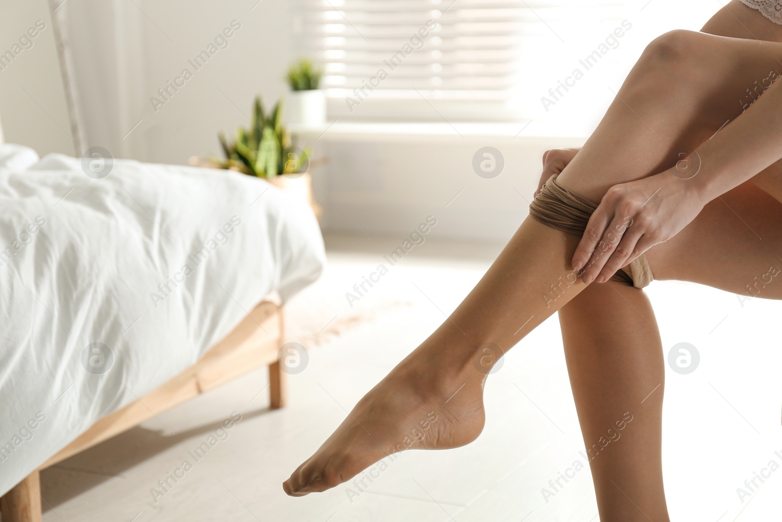 Photo of Young woman putting on tights in bedroom, closeup. Space for text