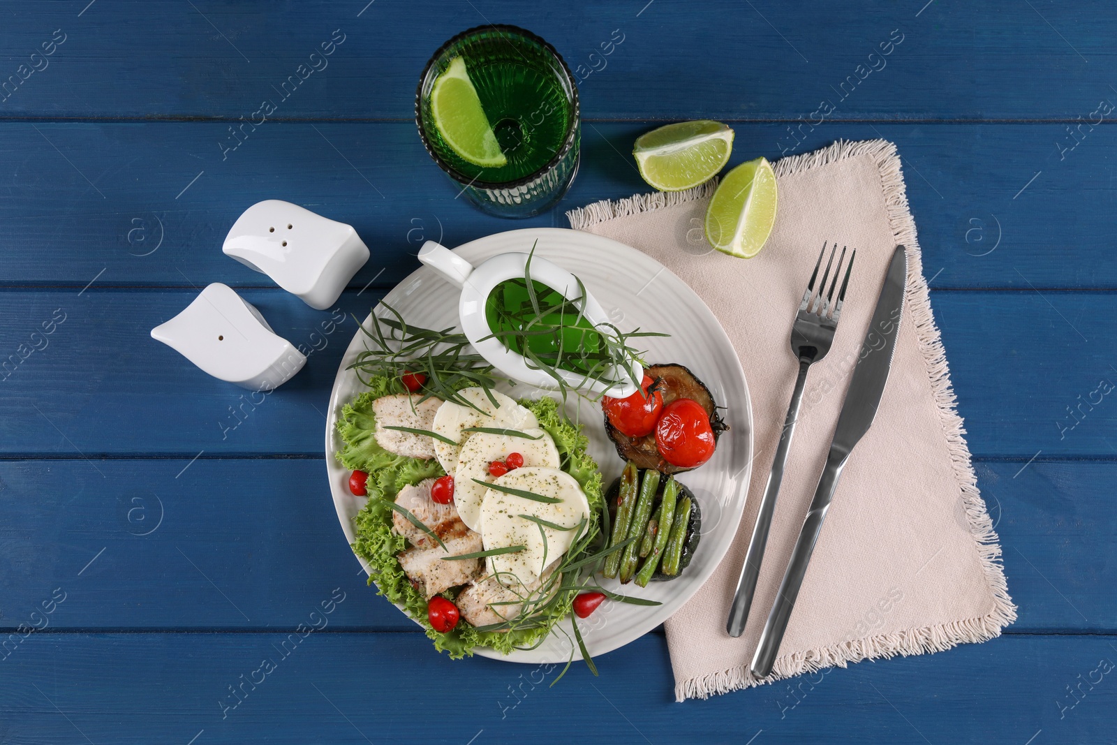 Photo of Tasty mozzarella, chicken, vegetables and drink with tarragon served on blue wooden table, flat lay